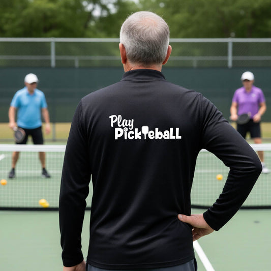 A man viewed from behind on a pickleball court, wearing a black long-sleeve shirt with the white text 'Play Pickleball' printed across the back. 