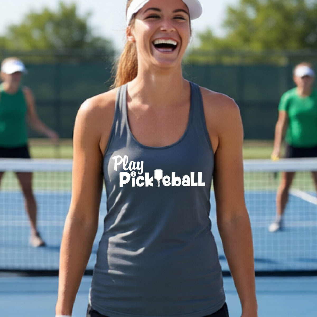 A woman on a pickleball court, wearing a gray racerback tank top with the white text 'Play Pickleball' across the back, including a pickleball paddle icon in place of the L in pickleball. 