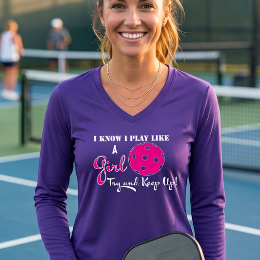 A woman laughing while wearing a purple long-sleeve v-neck  t-shirt with a pink and white graphic that reads 'I KNOW I PLAY LIKE A Girl Try and Keep Up!' with a pink pickleball illustration.