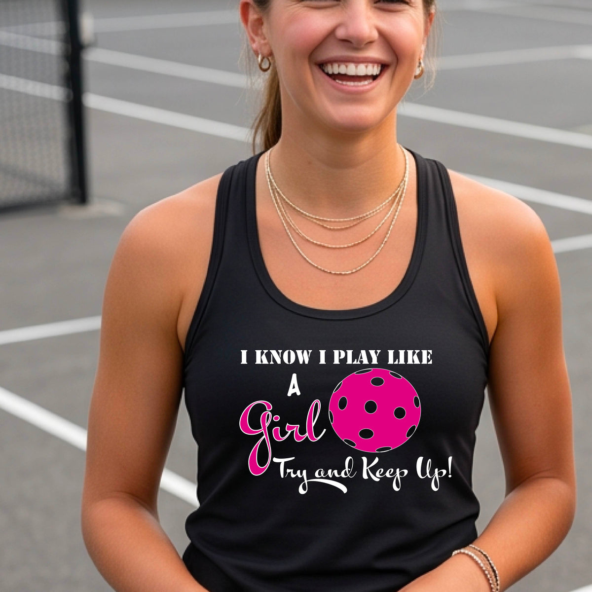A woman laughing while wearing a black racerback tank top with a pink and white graphic that reads 'I KNOW I PLAY LIKE A Girl Try and Keep Up!' with a pink pickleball illustration.