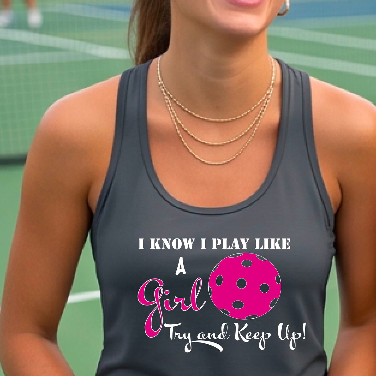 A woman laughing while wearing a dark gray racerback tank top with a pink and white graphic that reads 'I KNOW I PLAY LIKE A Girl Try and Keep Up!' with a pink pickleball illustration.