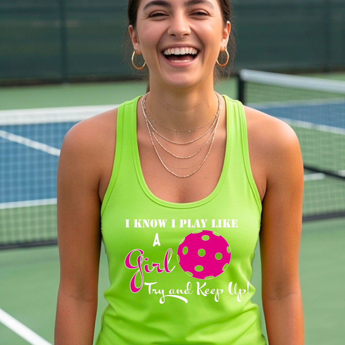 A woman laughing while wearing a lime green racerback tank top with a pink and white graphic that reads 'I KNOW I PLAY LIKE A Girl Try and Keep Up!' with a pink pickleball illustration.