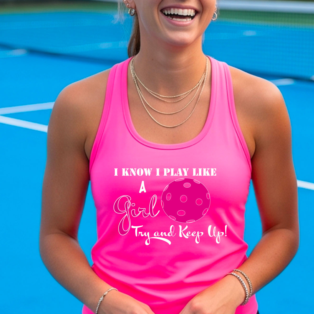 A woman laughing while wearing a pink racerback tank top with a pink and white graphic that reads 'I KNOW I PLAY LIKE A Girl Try and Keep Up!' with a pink pickleball illustration.