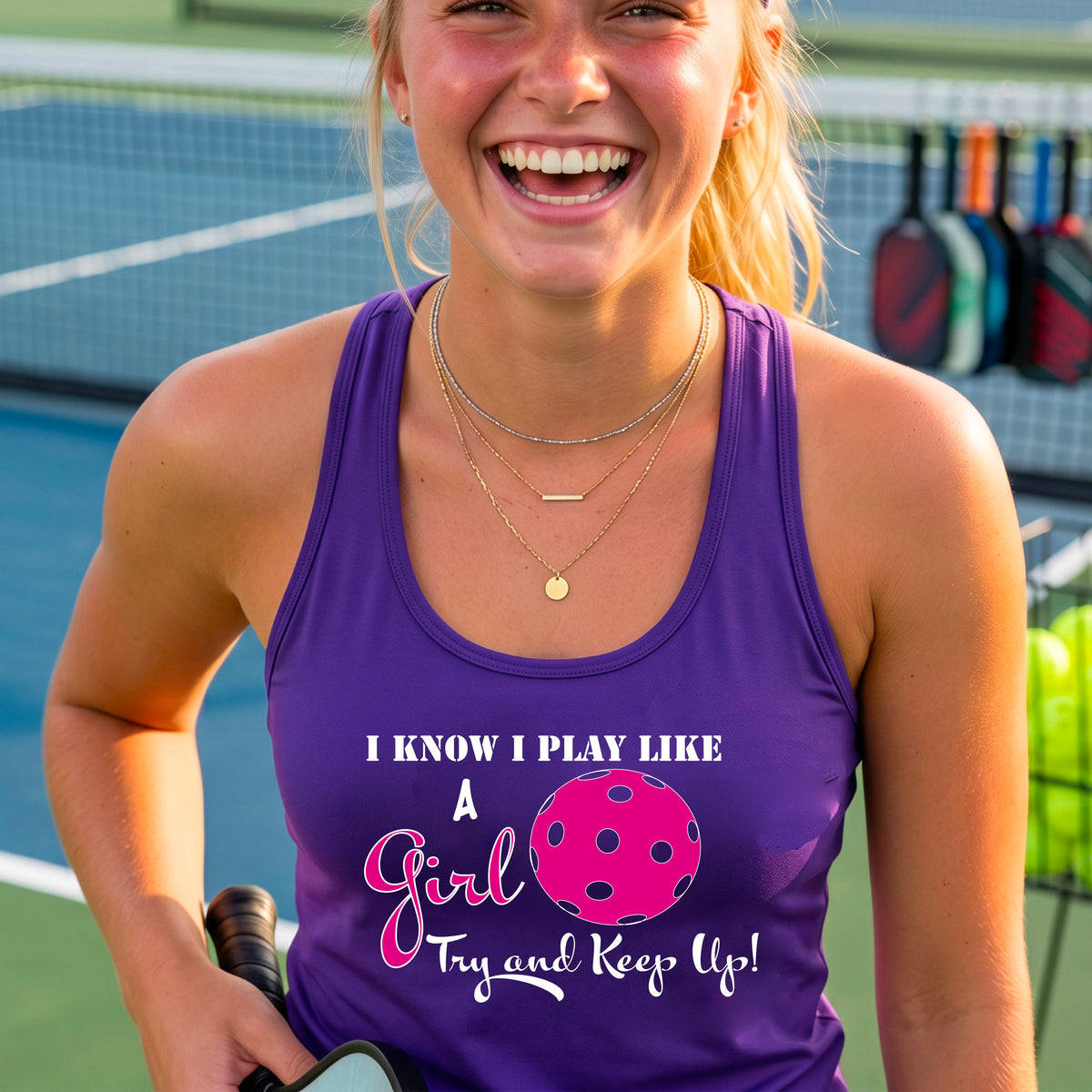 A woman laughing while wearing a purple racerback tank top with a pink and white graphic that reads 'I KNOW I PLAY LIKE A Girl Try and Keep Up!' with a pink pickleball illustration.