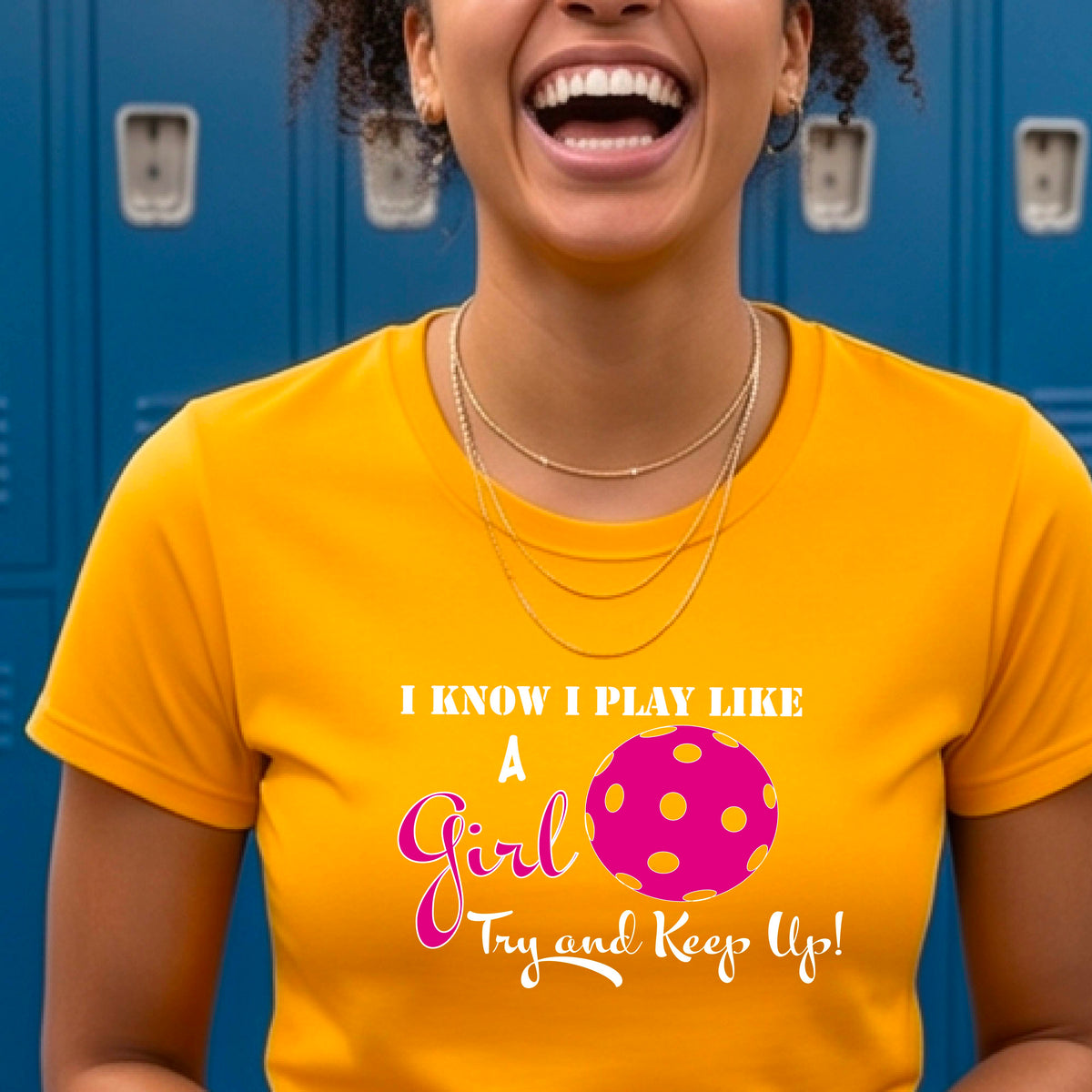 A woman laughing while wearing a gold short-sleeve t-shirt with a pink and white graphic that reads 'I KNOW I PLAY LIKE A Girl Try and Keep Up!' with a pink pickleball illustration.