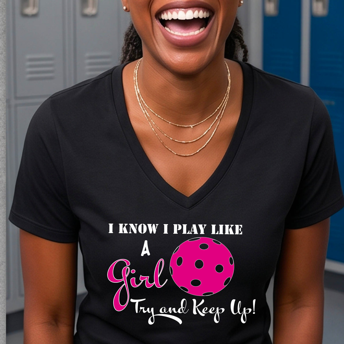 A woman laughing while wearing a black short-sleeve v-neck  t-shirt with a pink and white graphic that reads 'I KNOW I PLAY LIKE A Girl Try and Keep Up!' with a pink pickleball illustration.