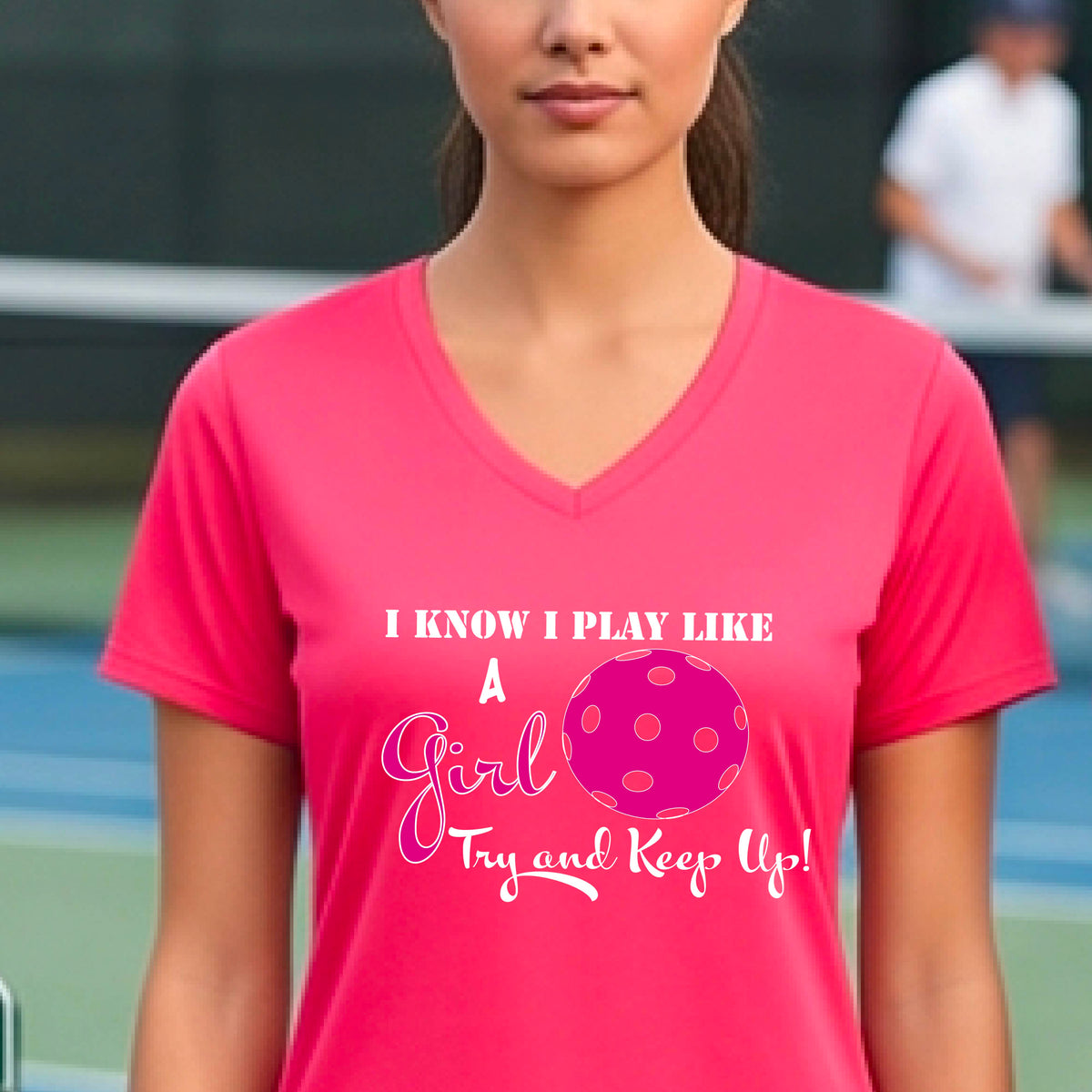 A woman laughing while wearing a pink short-sleeve v-neck  t-shirt with a pink and white graphic that reads 'I KNOW I PLAY LIKE A Girl Try and Keep Up!' with a pink pickleball illustration.