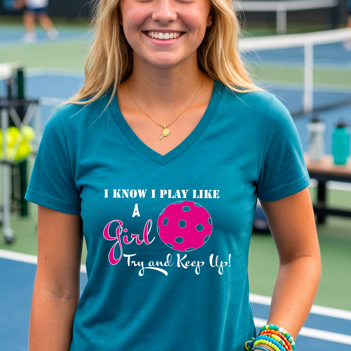 A woman laughing while wearing a teal short-sleeve v-neck  t-shirt with a pink and white graphic that reads 'I KNOW I PLAY LIKE A Girl Try and Keep Up!' with a pink pickleball illustration.