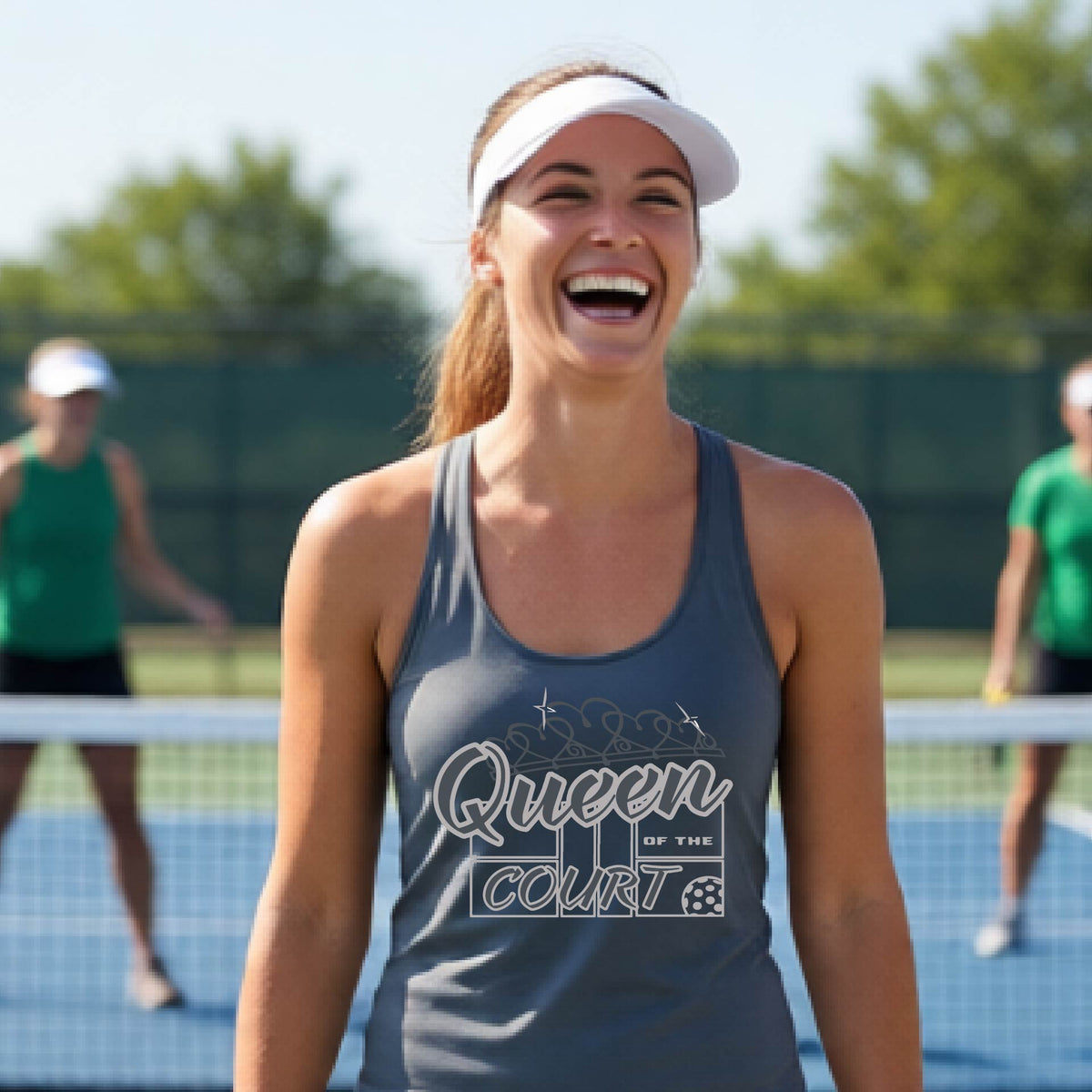 A woman laughing on a pickleball court, wearing a dark gray racerback tank top with a graphic that reads 'Queen of the Court' in gray and white and a pickleball graphic. 