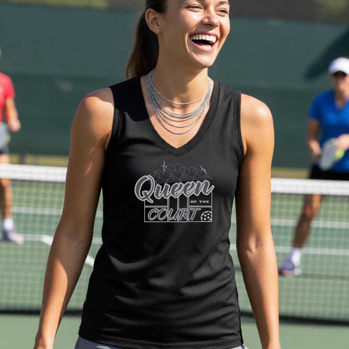 A woman laughing on a pickleball court wearing a black tank top with 'Queen Court' and a pickleball and court printed in gray script and block lettering on the front.