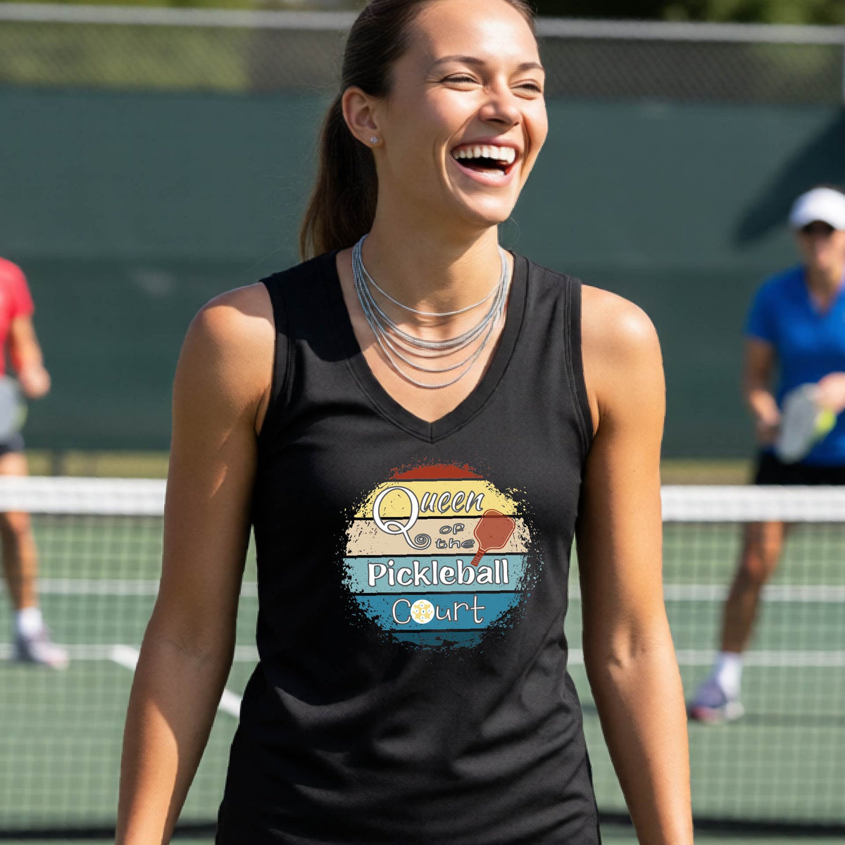 A woman on a pickleball court wearing a black sleeveless tank top with a colorful graphic that reads 'Queen of the Pickleball Court' in a retro sunset illustration.