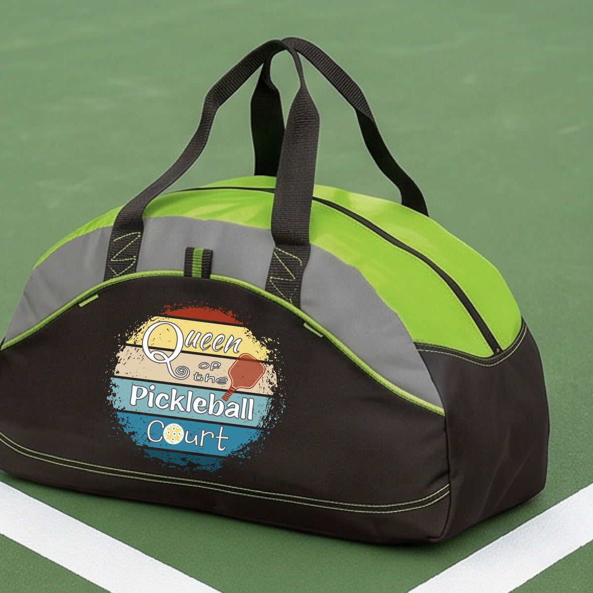 A custom pickleball duffel bag on a pickleball court, featuring a black and lime green color-blocked design with gray accents. The front has a custom graphic that reads 'Queen of hte Pickleball Court' with a pickleball illustration.