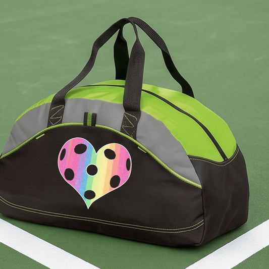 A close up of a medium size lime green and black duffel bag, with gray panels,  on a pickleball court, with a graphic of a brightly rainbow-colored heart designed like a pickleball on the front.