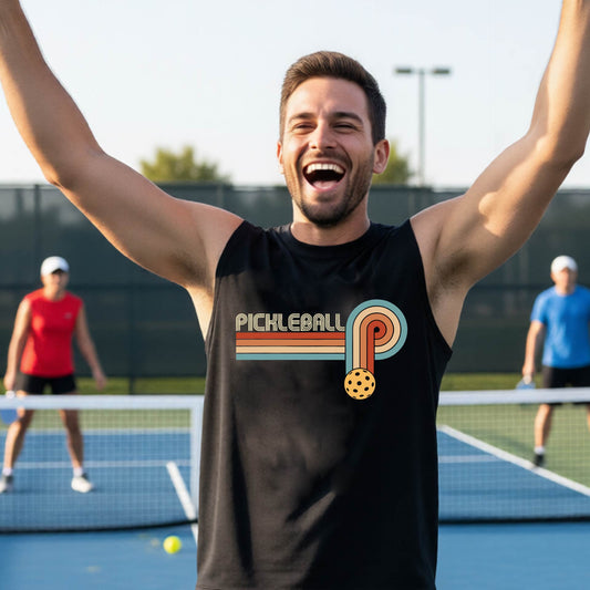 A man on a pickleball court wearing a black sleeveless t-shirt with a retro graphic of the word  “pickleball” on top of four colored lines that turn and go down ending in an orange pickleball, standing on a pickleball court.