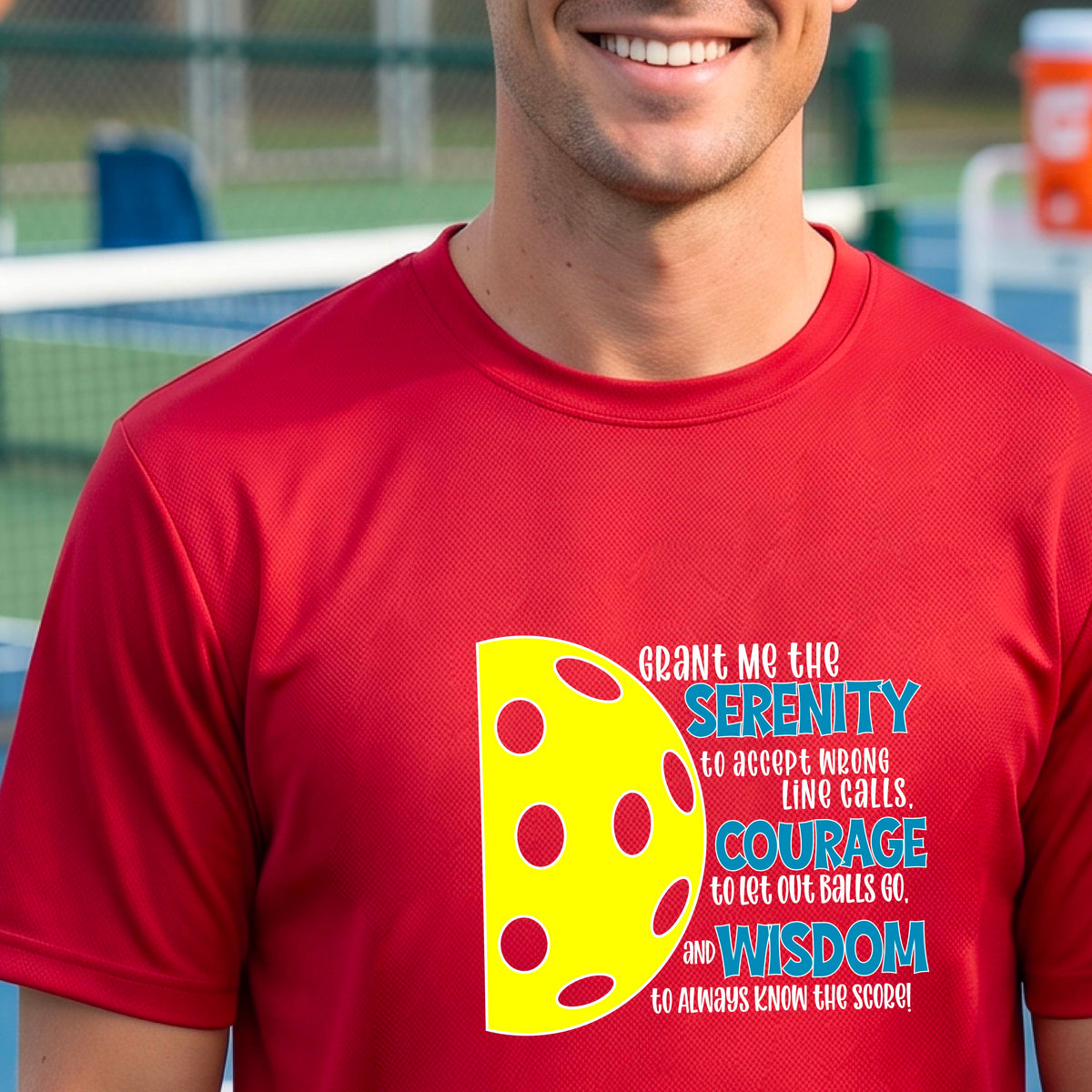 A man on a pickleball court wearing a red long-sleeve t-shirt with a graphic of the Serenity Prayer made for pickleball:  “Grant me the serenity to Accept Wrong Line Calls; Courage to Let Out Balls Go; and, Wisdom to Always Know the Score” next to a half-pickleball icon, standing on a pickleball court.