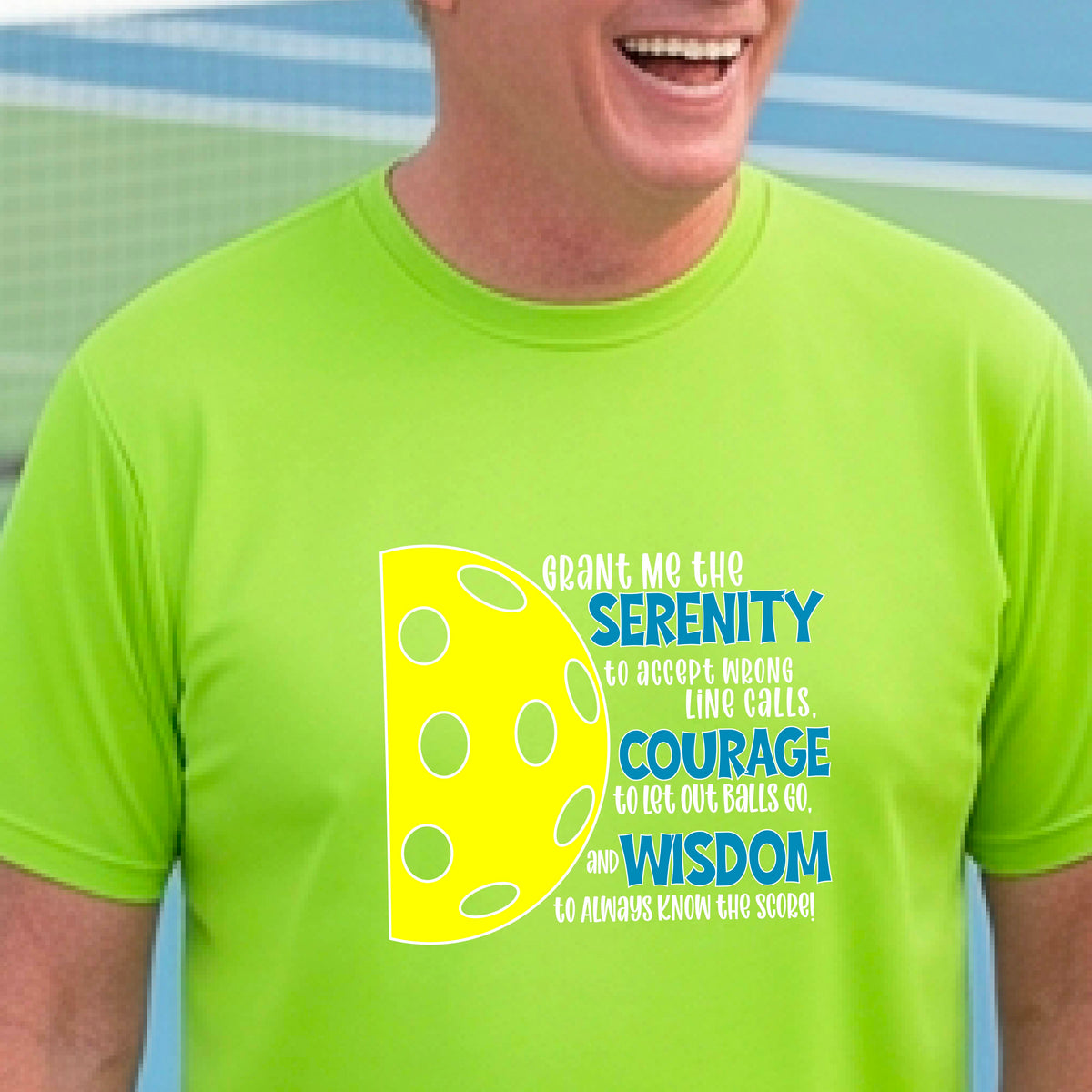 A man on a pickleball court wearing a lime green long-sleeve t-shirt with a graphic of the Serenity Prayer made for pickleball:  “Grant me the serenity to Accept Wrong Line Calls; Courage to Let Out Balls Go; and, Wisdom to Always Know the Score” next to a half-pickleball icon, standing on a pickleball court.