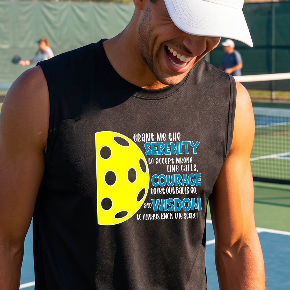 A man on a pickleball court wearing a black sleeveless t-shirt with a graphic of the Serenity Prayer made for pickleball:  “Grant me the serenity to Accept Wrong Line Calls; Courage to Let Out Balls Go; and, Wisdom to Always Know the Score” next to a half-pickleball icon, standing on a pickleball court.