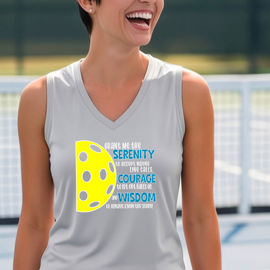 A woman on a pickleball court wearing a gray sleeveless t-shirt with a graphic of the Serenity Prayer made for pickleball:  “Grant me the serenity to Accept Wrong Line Calls; Courage to Let Out Balls Go; and, Wisdom to Always Know the Score” next to a half-pickleball icon, standing on a pickleball court.
