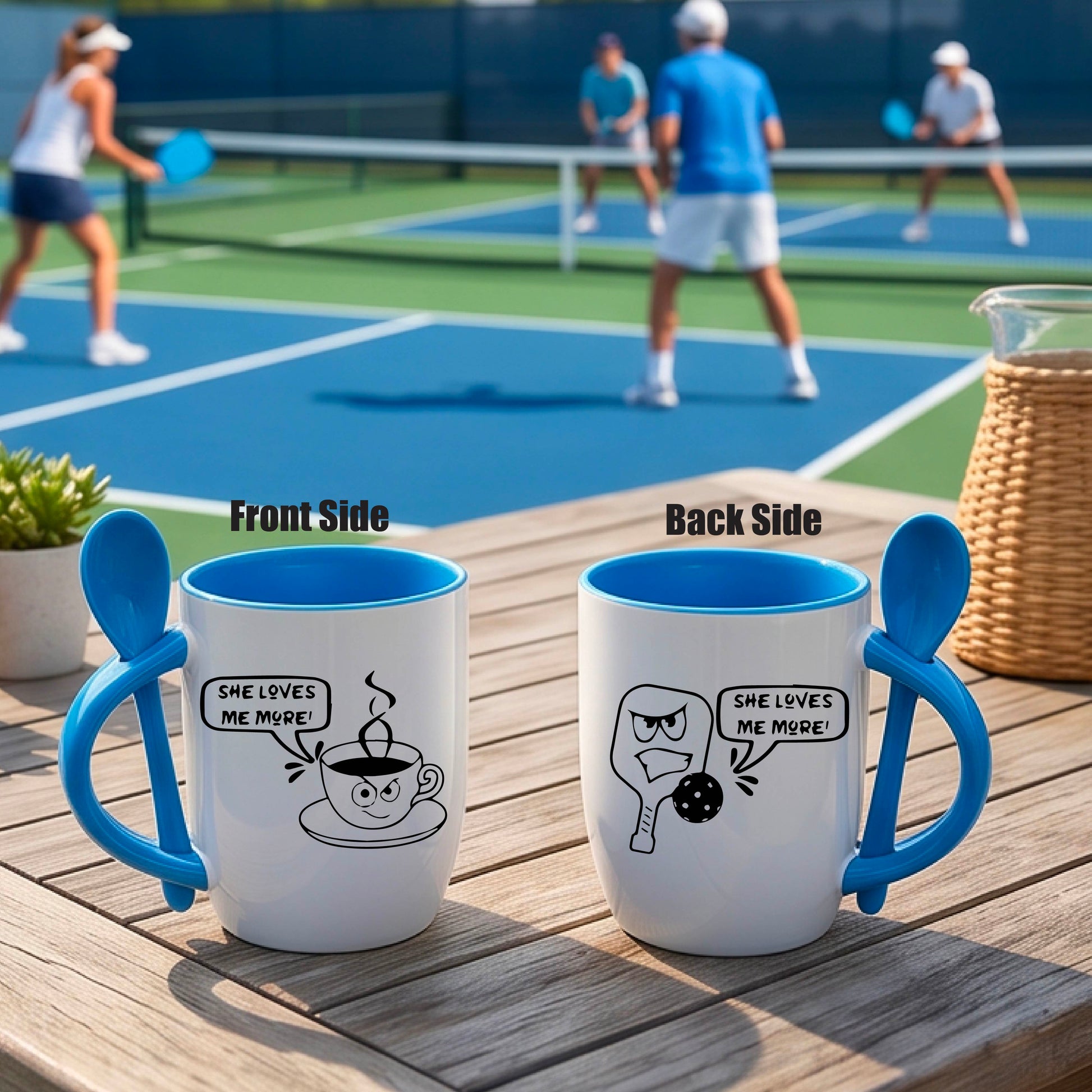 A white and blue 12 ounce coffee mug with a built in spoon in the handle with and a fun pickleball paddle and ball and coffee cup graphic and the text “SHE LOVES ME MORE”