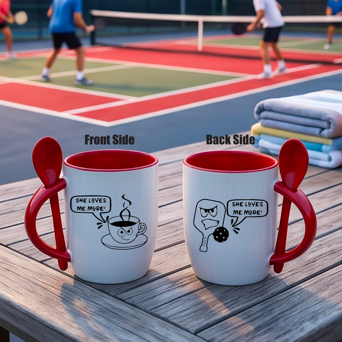 A white and red 12 ounce coffee mug with a built in spoon in the handle with and a fun pickleball paddle and ball and coffee cup graphic and the text “SHE LOVES ME MORE”
