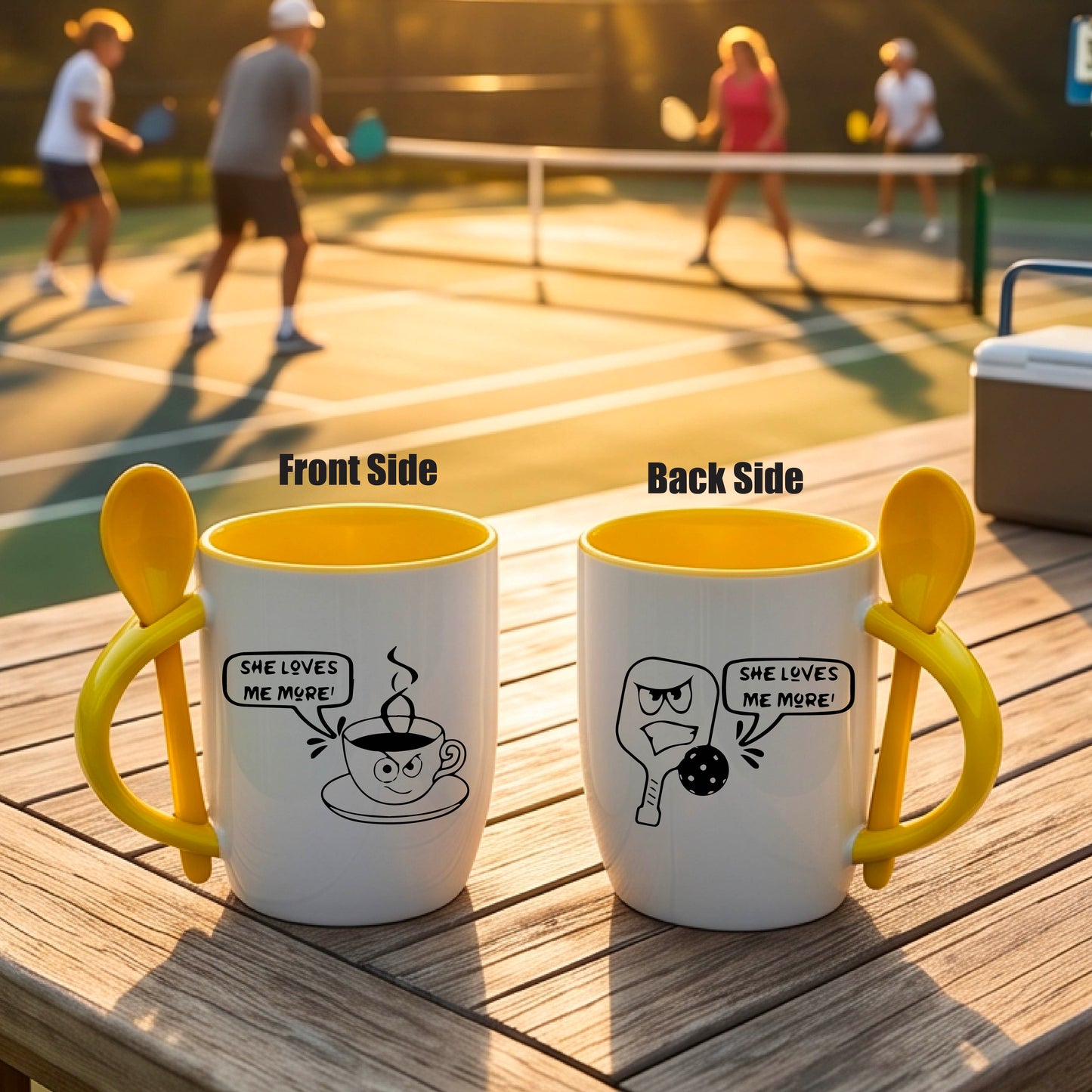 A white and yellow 12 ounce coffee mug with a built in spoon in the handle with and a fun pickleball paddle and ball and coffee cup graphic and the text “SHE LOVES ME MORE”