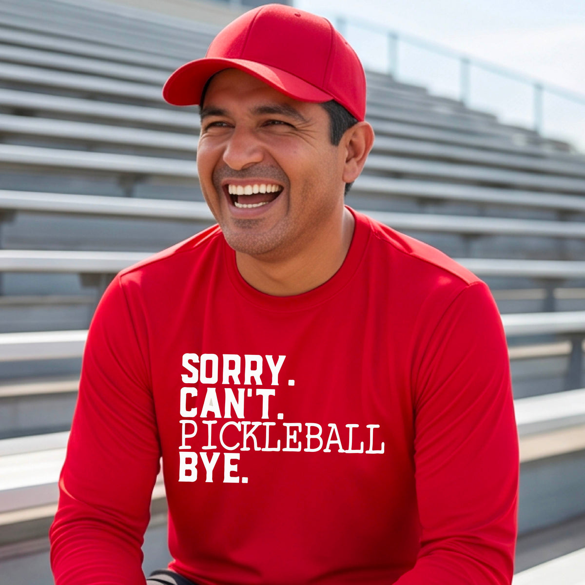 A man wearing a red long-sleeve t-shirt with a white graphic of the words  “SORRY. CAN’T. PICKLEBALL BYE” each on a separate line, on the front of the shirt. 
