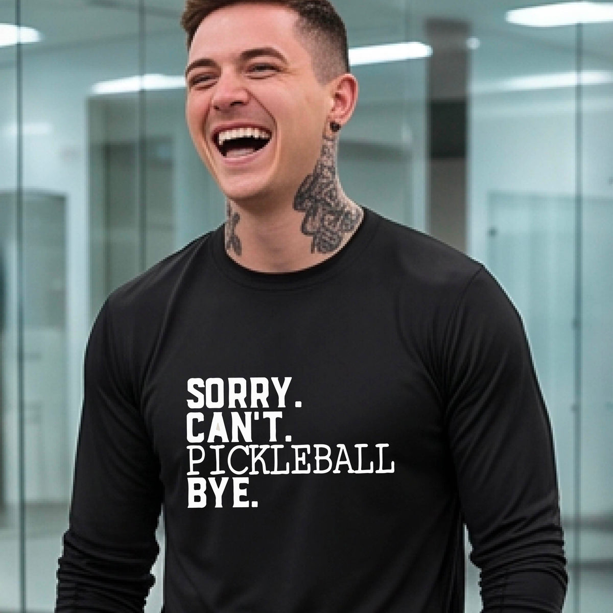 A man wearing a black long-sleeve t-shirt with a white graphic of the words  “SORRY. CAN’T. PICKLEBALL BYE” each on a separate line, on the front of the shirt. 