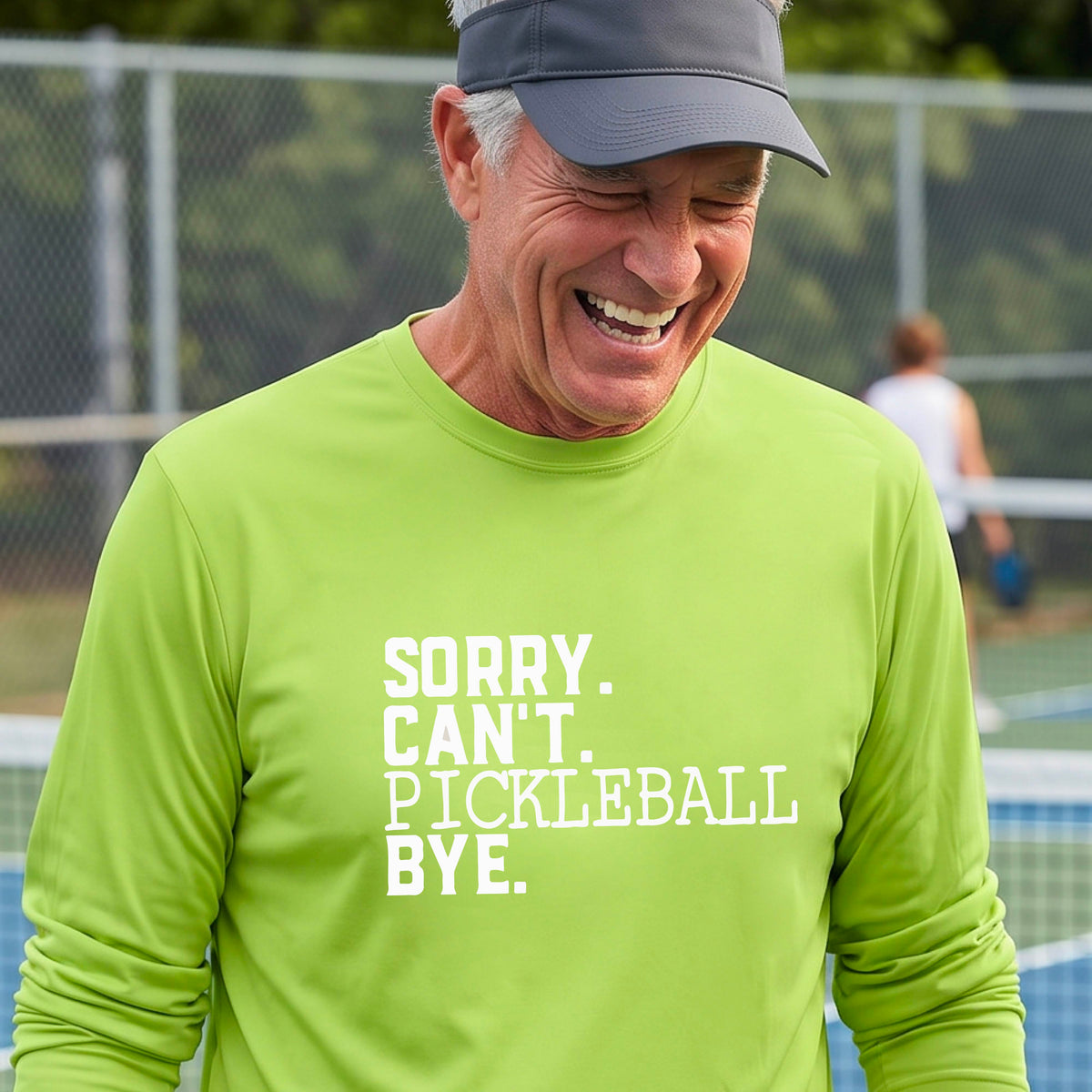 A man on a pickleball court wearing a lime green long-sleeve t-shirt with a white graphic of the words  “SORRY. CAN’T. PICKLEBALL BYE” each on a separate line, on the front of the shirt. 