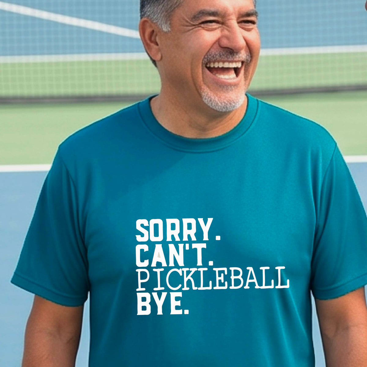 A man on a pickleball court wearing a teal short-sleeve t-shirt with a white graphic of the words  “SORRY. CAN’T. PICKLEBALL BYE” each on a separate line, on the front of the shirt. 
