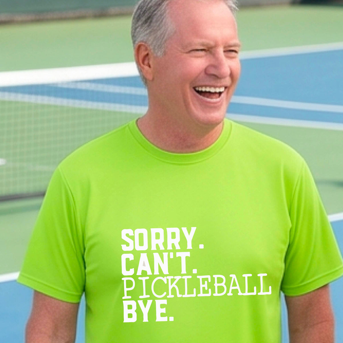 A man on a pickleball court wearing a lime green short-sleeve t-shirt with a white graphic of the words  “SORRY. CAN’T. PICKLEBALL BYE” each on a separate line, on the front of the shirt. 