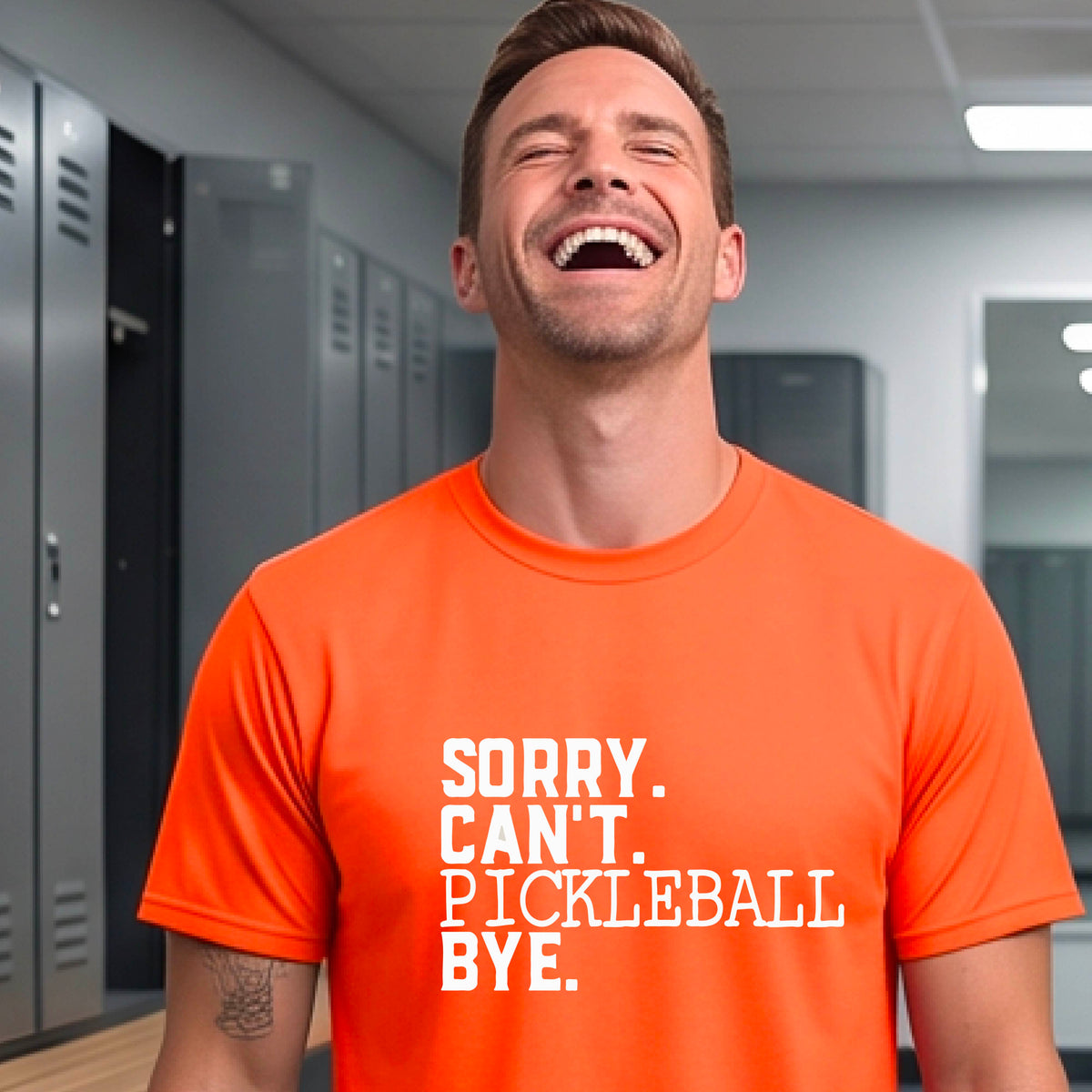 A man wearing an orange short-sleeve t-shirt with a white graphic of the words  “SORRY. CAN’T. PICKLEBALL BYE” each on a separate line, on the front of the shirt. 