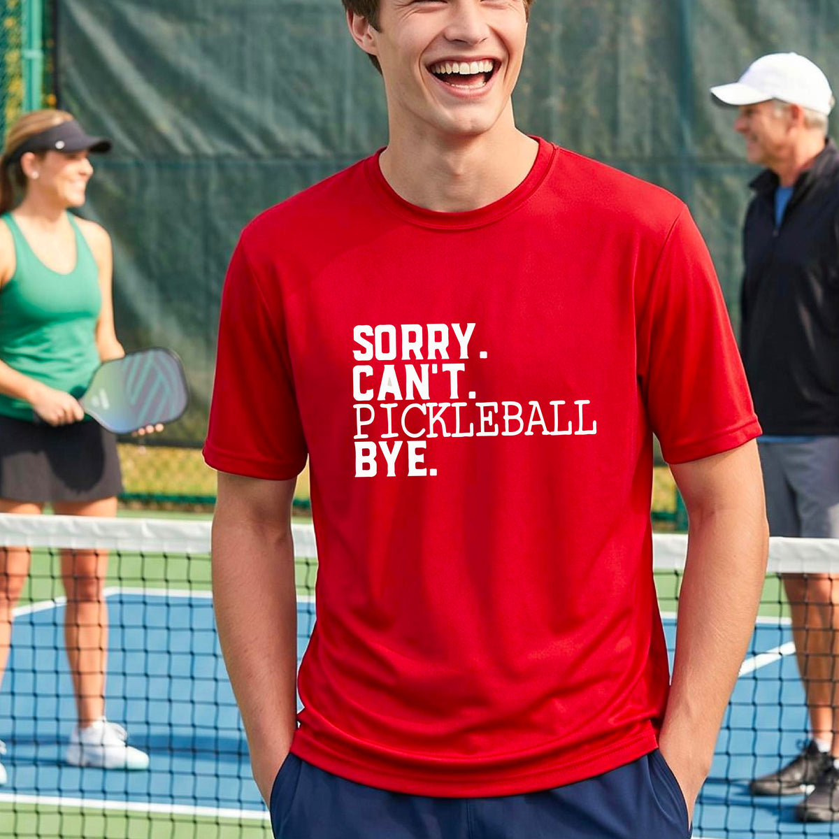 A man on a pickleball court wearing a red short-sleeve t-shirt with a white graphic of the words  “SORRY. CAN’T. PICKLEBALL BYE” each on a separate line, on the front of the shirt. 