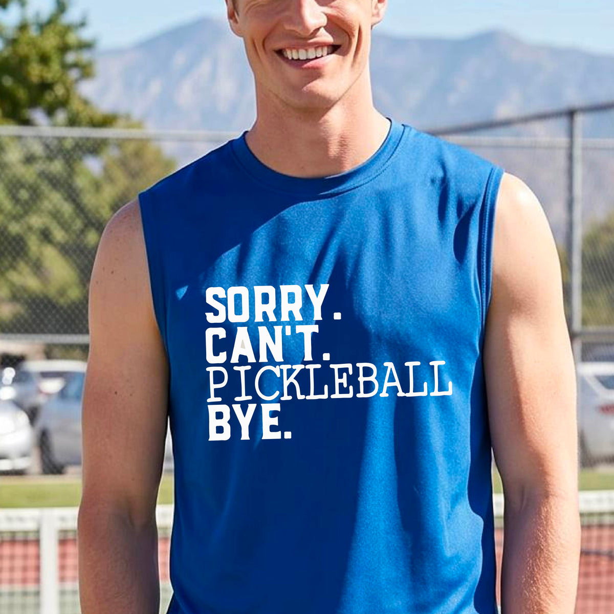 A man on a pickleball court wearing a royal blue sleeveless t-shirt with a white graphic of the words  “SORRY. CAN’T. PICKLEBALL BYE” each on a separate line, on the front of the shirt. 