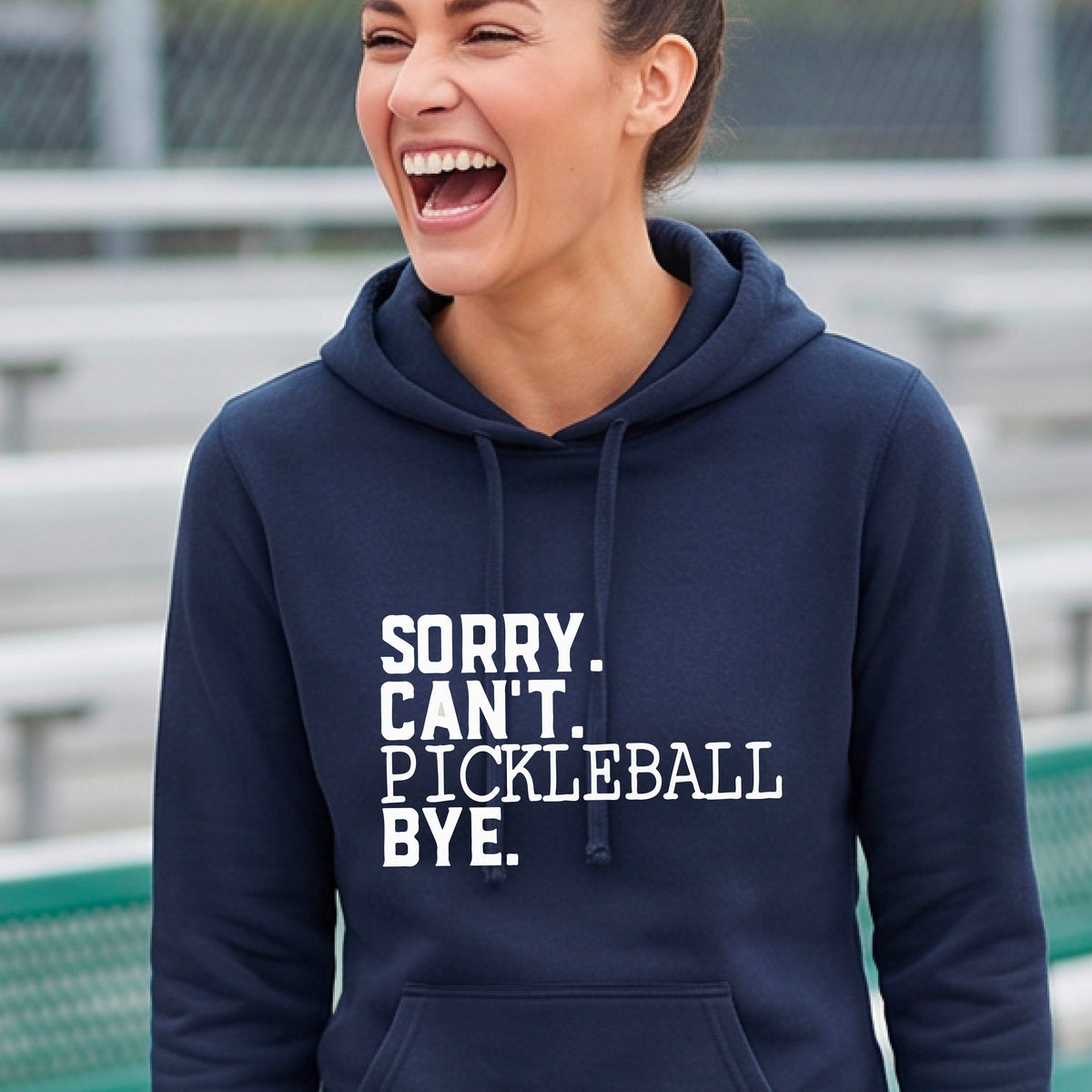 A woman on a pickleball court wearing a navy blue short-sleeve t-shirt with a white graphic of the words  “SORRY. CAN’T. PICKLEBALL BYE” each on a separate line, on the front of the shirt. 