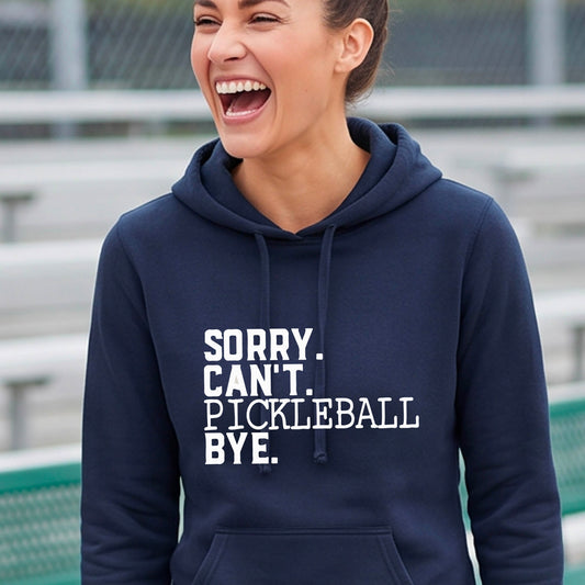 A woman on a pickleball court wearing a navy blue short-sleeve t-shirt with a white graphic of the words  “SORRY. CAN’T. PICKLEBALL BYE” each on a separate line, on the front of the shirt. 