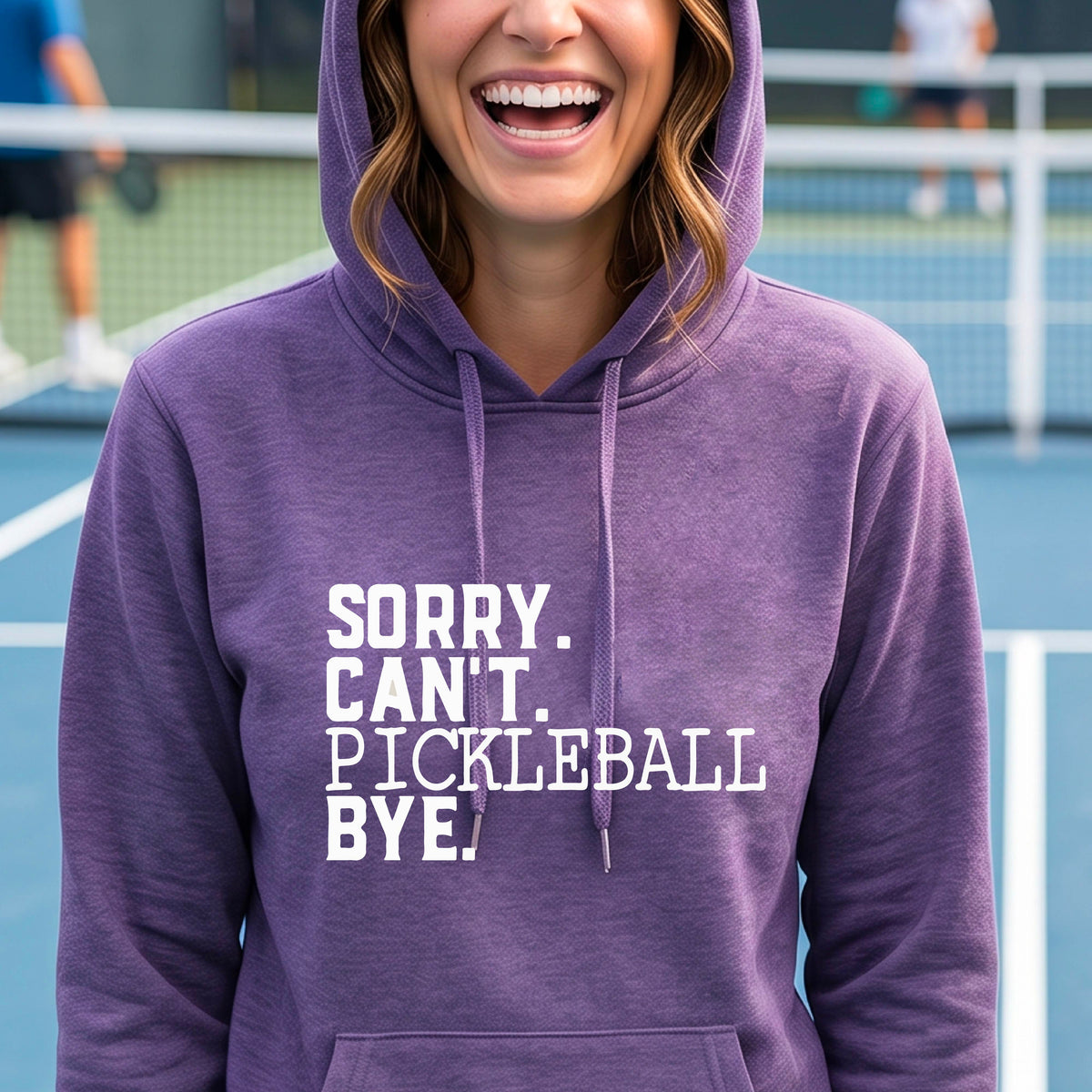 A woman on a pickleball court wearing a purple short-sleeve t-shirt with a white graphic of the words  “SORRY. CAN’T. PICKLEBALL BYE” each on a separate line, on the front of the shirt. 