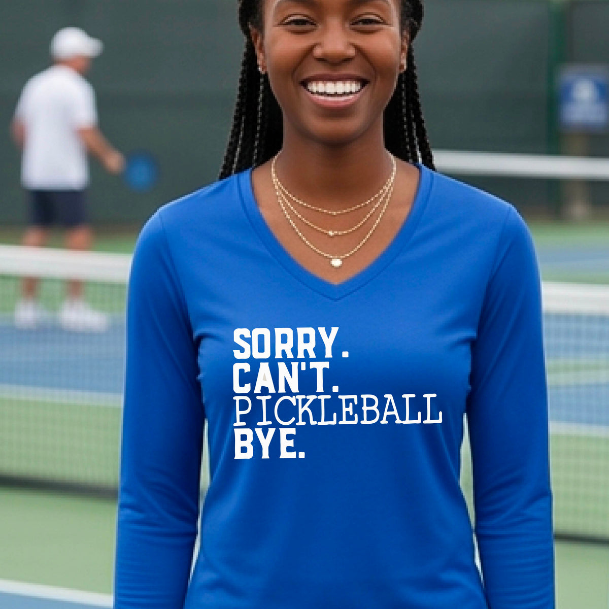 A woman on a pickleball court wearing a royal blue long-sleeve t-shirt with a white graphic of the words  “SORRY. CAN’T. PICKLEBALL BYE” each on a separate line, on the front of the shirt. 