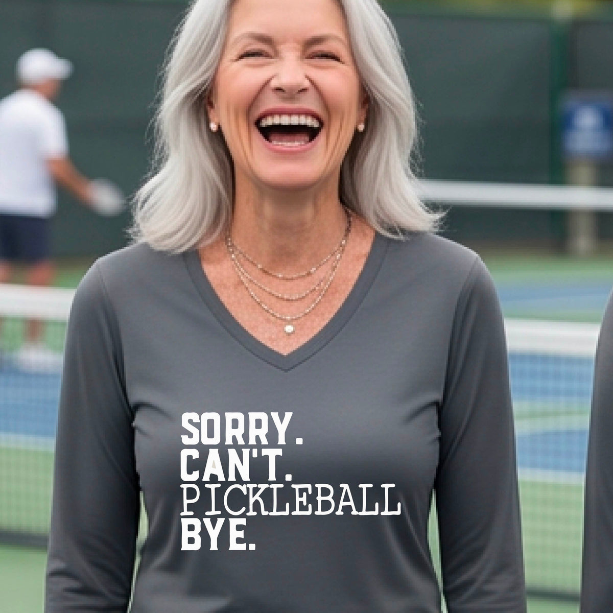 A woman on a pickleball court wearing a dark gray long-sleeve t-shirt with a white graphic of the words  “SORRY. CAN’T. PICKLEBALL BYE” each on a separate line, on the front of the shirt. 