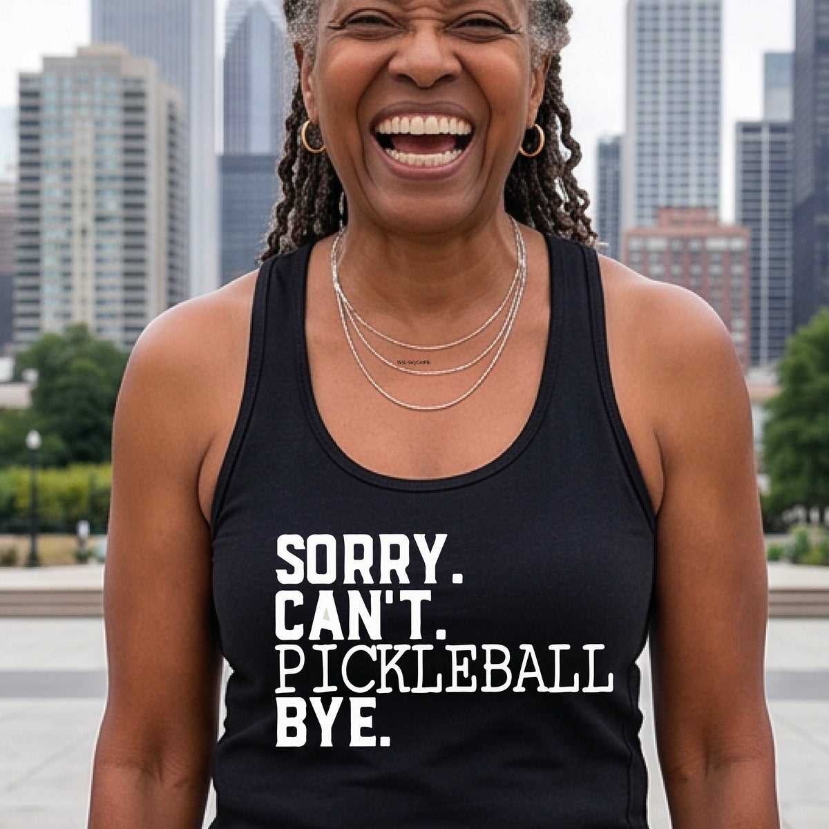 A woman on a pickleball court wearing a black racerback tank top with a white graphic of the words  “SORRY. CAN’T. PICKLEBALL BYE” each on a separate line, on the fron of the shirt. 
