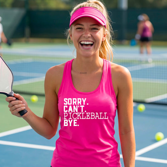 A woman on a pickleball court wearing a pink racerback tank top with a white graphic of the words  “SORRY. CAN’T. PICKLEBALL BYE” each on a separate line, on the fron of the shirt. 