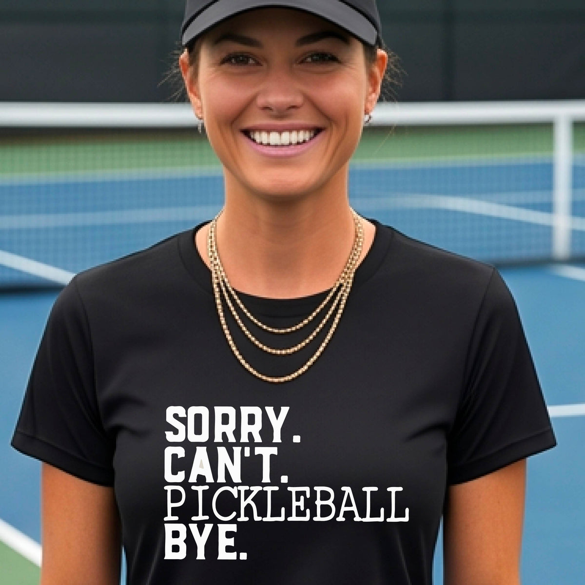 A woman on a pickleball court wearing a black short-sleeve t-shirt with a white graphic of the words  “SORRY. CAN’T. PICKLEBALL BYE” each on a separate line, on the front of the shirt. 