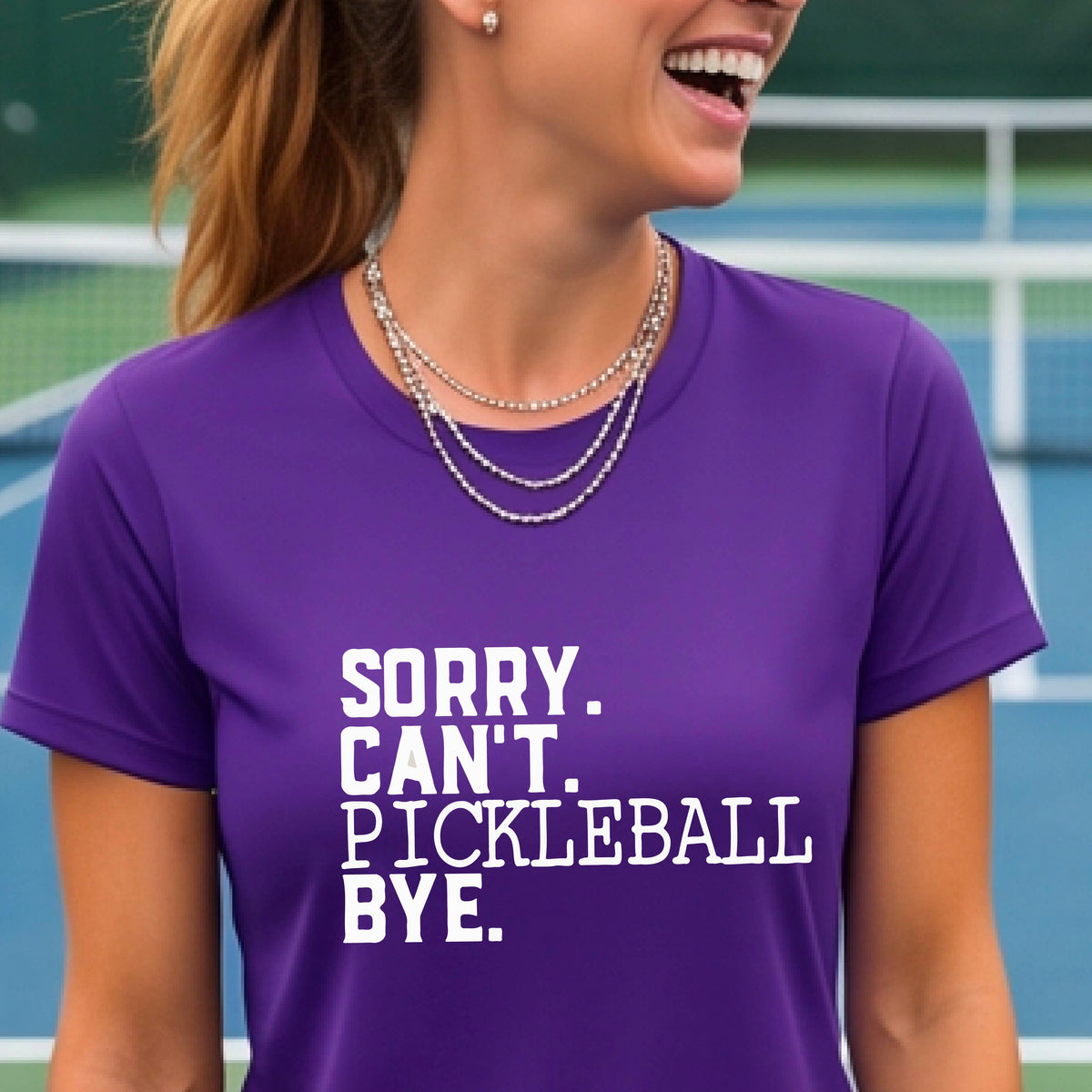 A woman on a pickleball court wearing a purple short-sleeve t-shirt with a white graphic of the words  “SORRY. CAN’T. PICKLEBALL BYE” each on a separate line, on the front of the shirt. 

