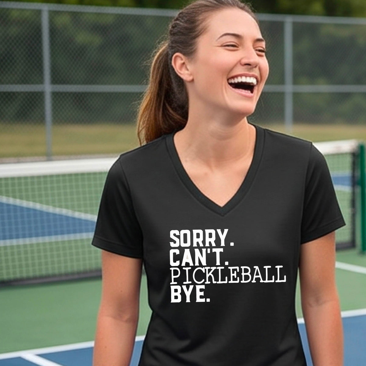 A woman on a pickleball court wearing a black short-sleeve t-shirt with a white graphic of the words  “SORRY. CAN’T. PICKLEBALL BYE” each on a separate line, on the front of the shirt. 