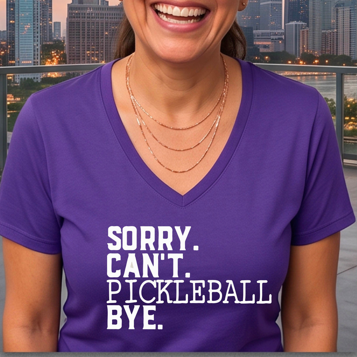 A woman on a pickleball court wearing a purple short-sleeve t-shirt with a white graphic of the words  “SORRY. CAN’T. PICKLEBALL BYE” each on a separate line, on the front of the shirt. 