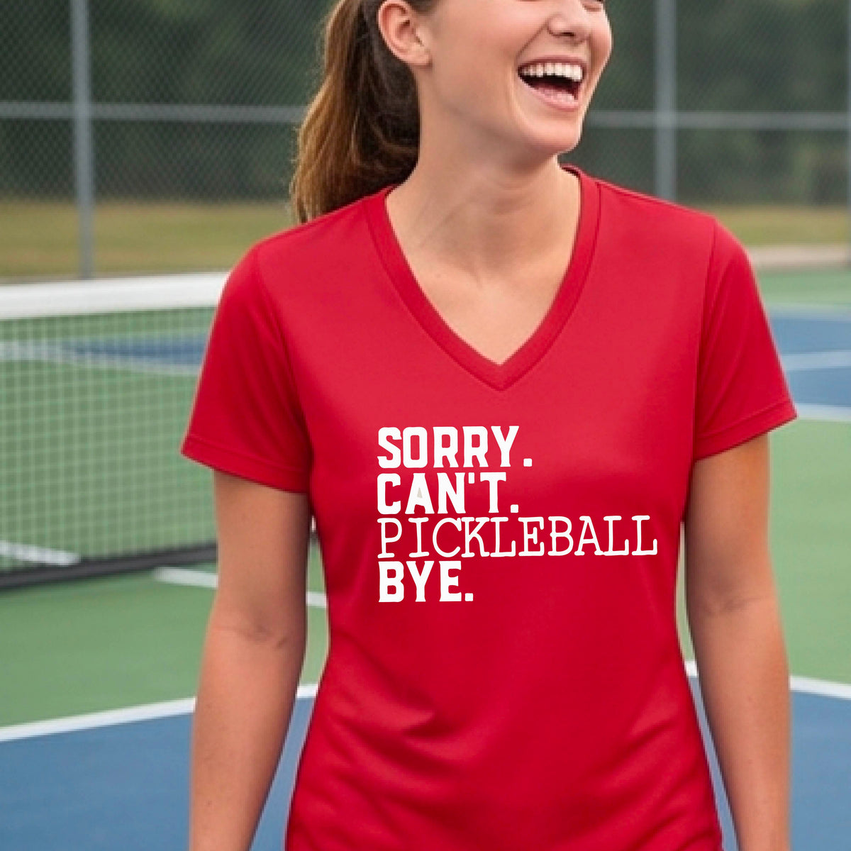 A woman on a pickleball court wearing a red short-sleeve t-shirt with a white graphic of the words  “SORRY. CAN’T. PICKLEBALL BYE” each on a separate line, on the front of the shirt. 