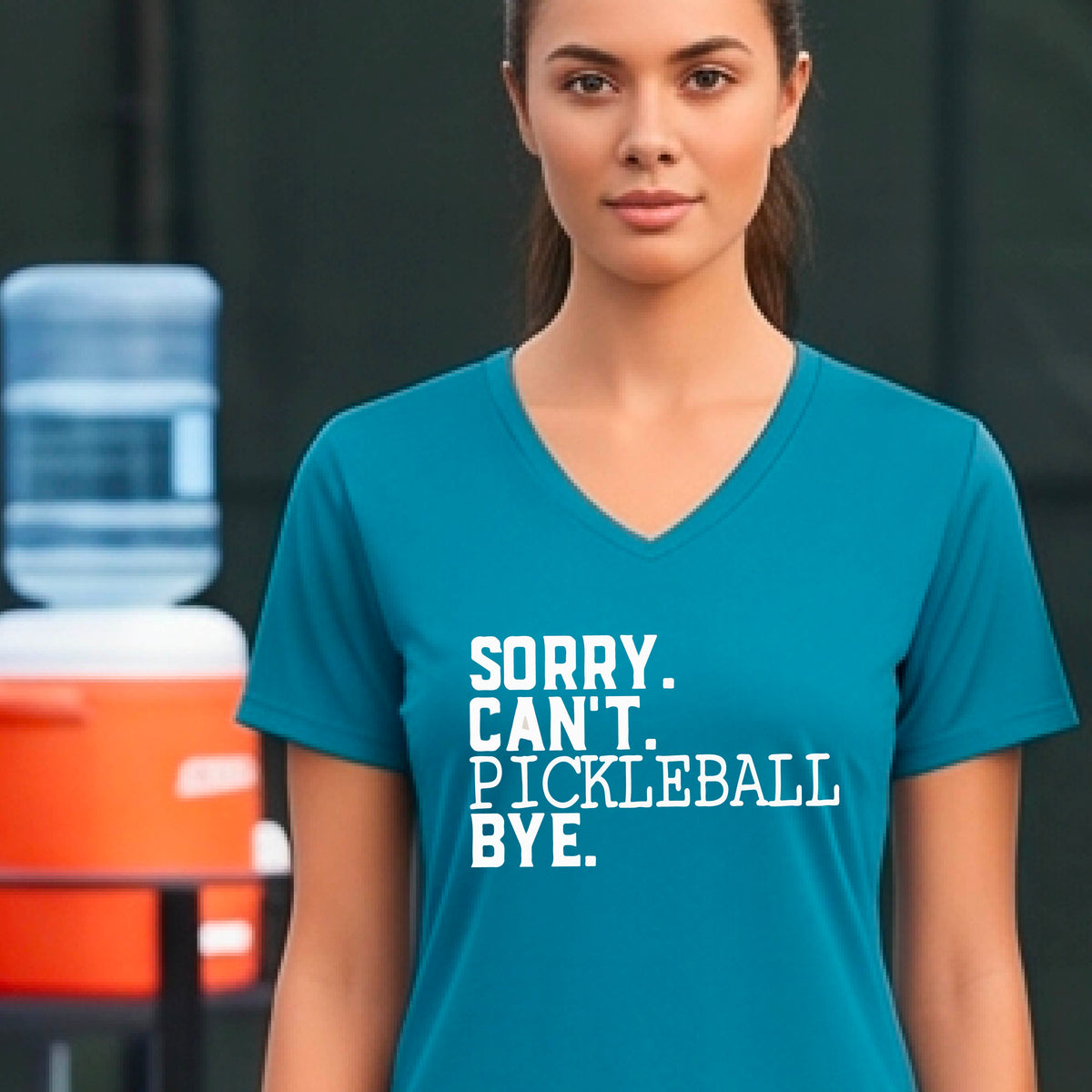 A woman on a pickleball court wearing a teal short-sleeve t-shirt with a white graphic of the words  “SORRY. CAN’T. PICKLEBALL BYE” each on a separate line, on the front of the shirt. 