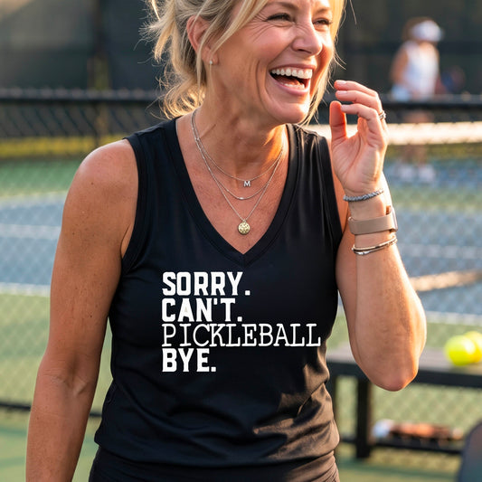 A woman on a pickleball court wearing a black sleeveless t-shirt with a white graphic of the words  “SORRY. CAN’T. PICKLEBALL BYE” each on a separate line, on the front of the shirt. 


