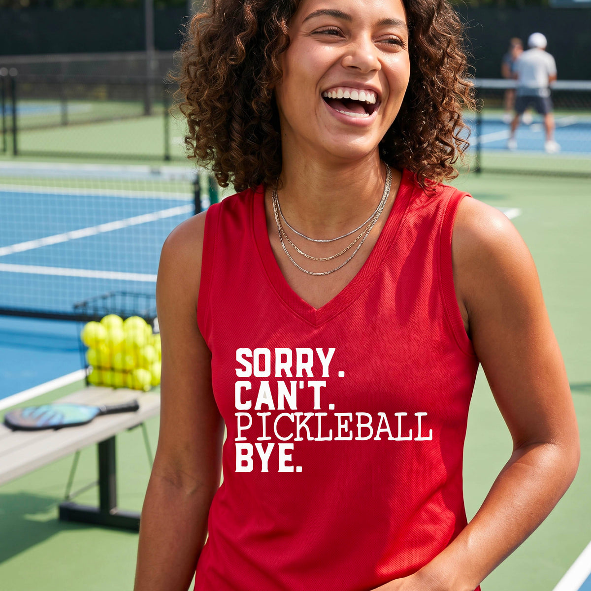 A woman on a pickleball court wearing a red sleeveless t-shirt with a white graphic of the words  “SORRY. CAN’T. PICKLEBALL BYE” each on a separate line, on the front of the shirt. 
