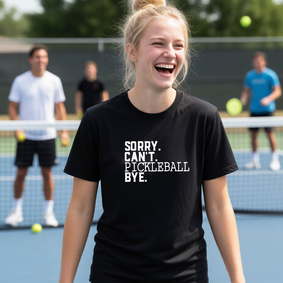 A young person on a pickleball court wearing a black short-sleeve t-shirt with a white graphic of the words  “SORRY. CAN’T. PICKLEBALL BYE” each on a separate line, on the front of the shirt. 