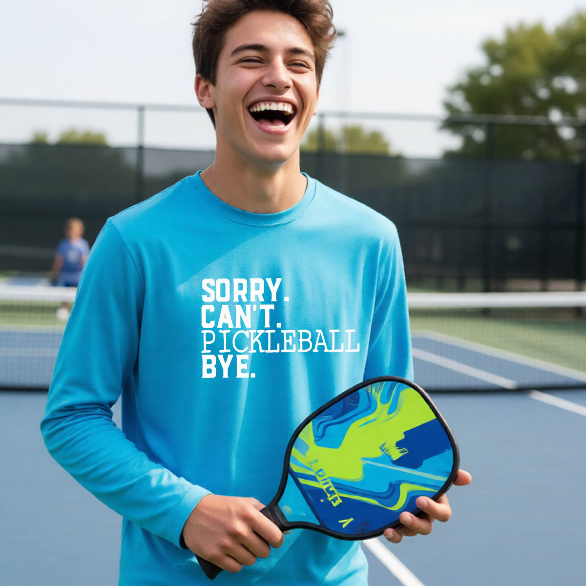 A young person on a pickleball court wearing a bright blue short-sleeve t-shirt with a white graphic of the words  “SORRY. CAN’T. PICKLEBALL BYE” each on a separate line, on the front of the shirt.